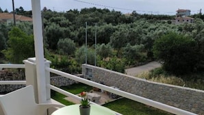 A balcony with a small table and two chairs, overlooking a garden and a stone wall.