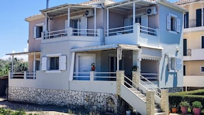A two-story building with a stone base, a balcony on the upper floor, and a small staircase leading to the entrance.
