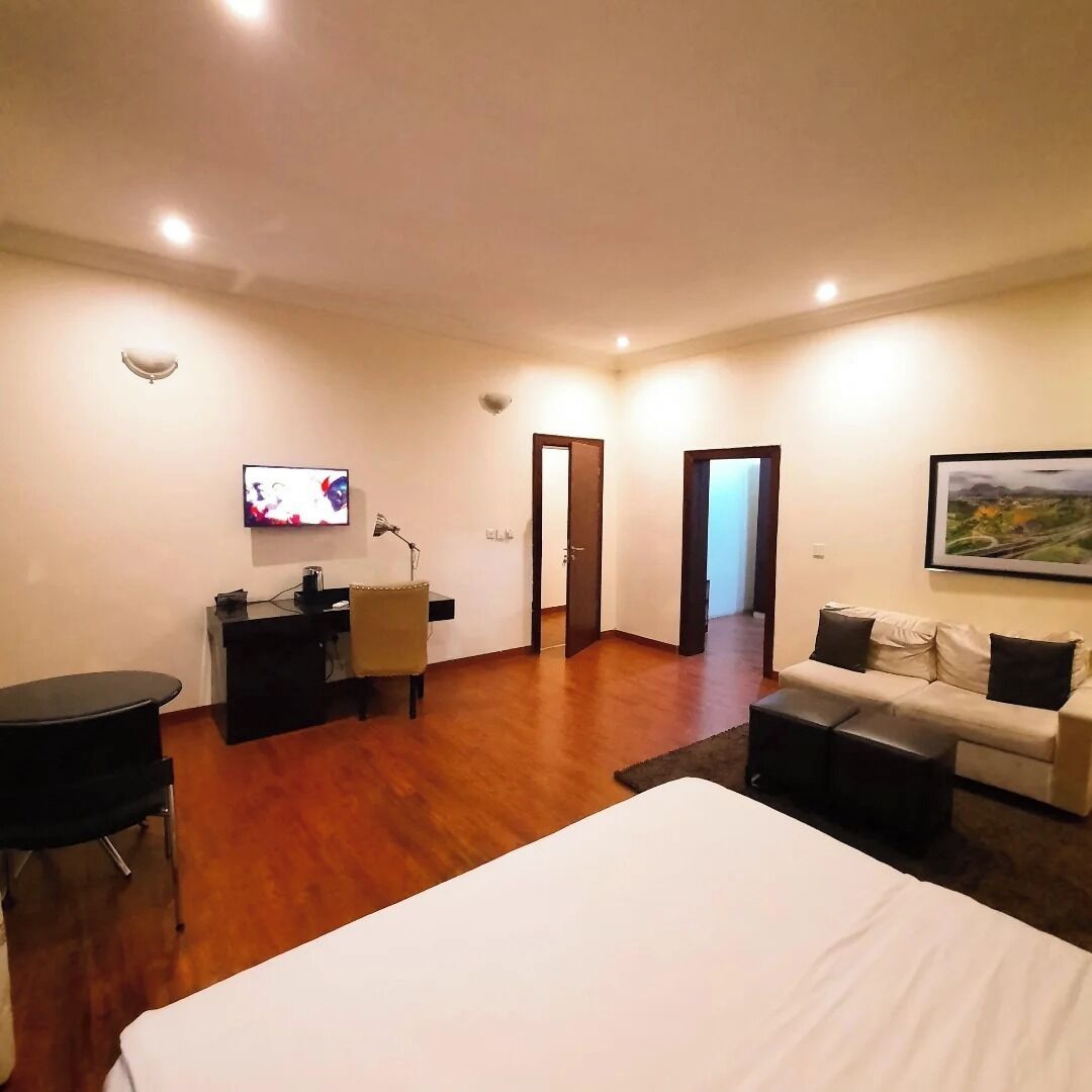 A spacious room with a large bed, a desk with a chair, a sofa, and a television mounted on the wall.