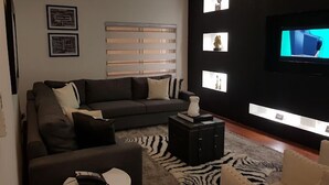 A modern living room with a dark sofa, a small round table, a zebra-patterned rug, and a TV mounted on a black wall with illuminated shelves. - NiCotel Apartments (Abuja)
