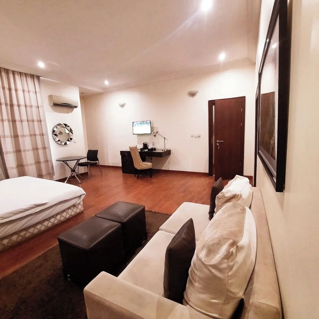 A hotel room with a bed, a sofa, a desk with a chair, a TV, and a door.