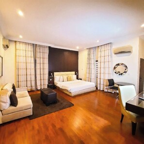 A modern hotel room with a large bed, a sofa, a small table, and a chair. - NiCotel Apartments (Abuja)
