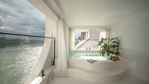 Ein moderner Balkon mit Blick auf einen Fluss und Gebäude, ausgestattet mit einem Whirlpool und einem Blumentopf.