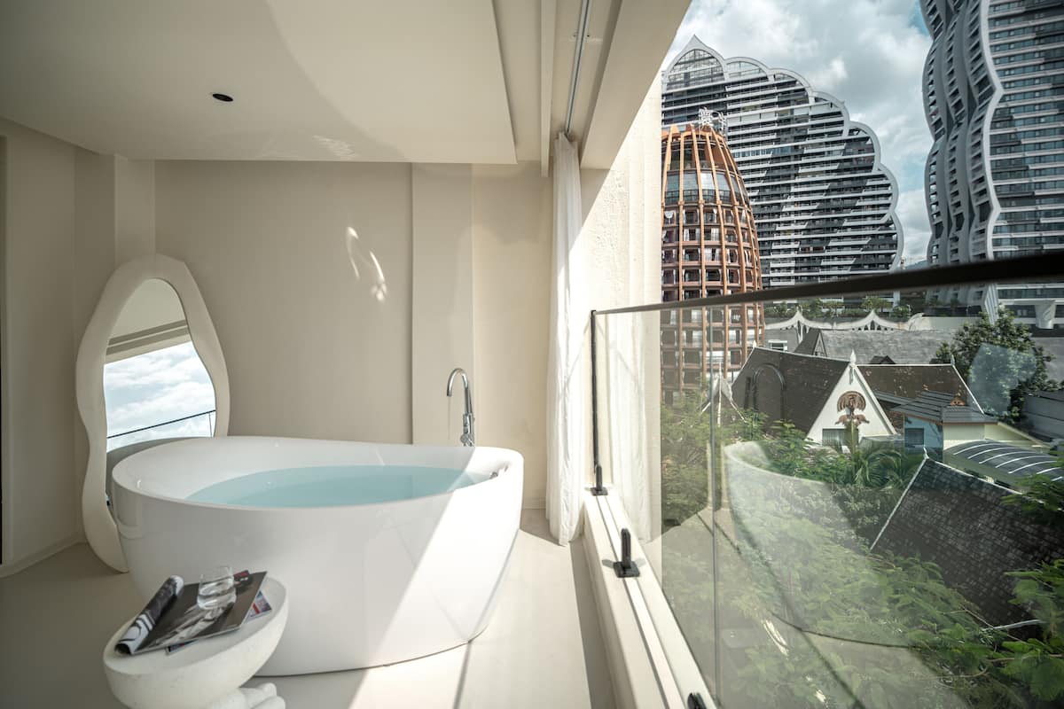 Une salle de bain moderne avec une baignoire sur pieds, un grand miroir et une vue sur le paysage urbain grâce à un balcon en verre.