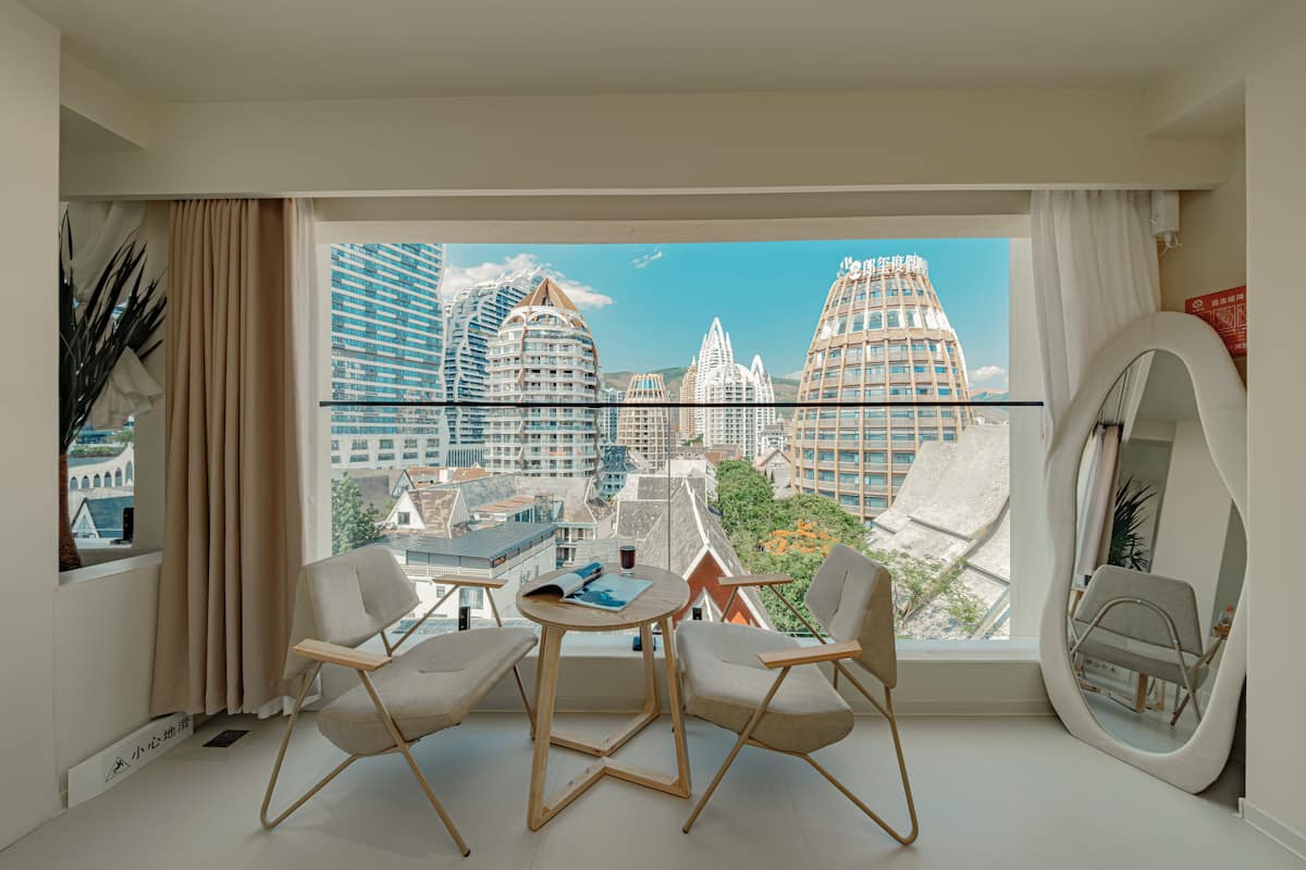 Une chambre moderne dotée d’une grande fenêtre donnant sur la ville, d’une table ronde, de deux chaises et d’un miroir.