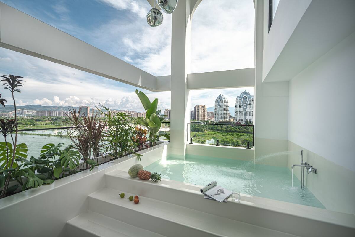 Une salle de bain moderne avec une grande baignoire, une vue sur le paysage urbain et diverses plantes.