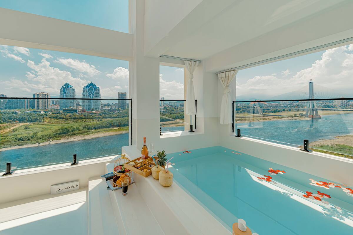 Une chambre d’hôtel moderne dotée d’une grande fenêtre donnant sur un paysage urbain et une rivière.