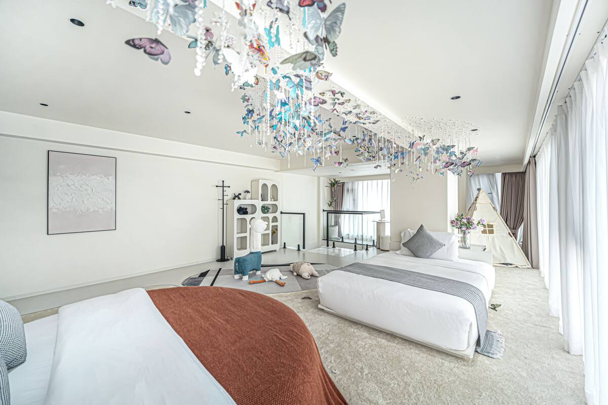 Une chambre d’hôtel moderne avec deux lits, une grande fenêtre et un plafond décoré de motifs représentant des papillons.