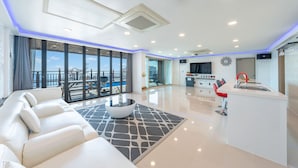 A modern living room with a white sofa, a coffee table, and a view of the sea through large windows. - Pohang Blue Hill Pension (Pohang)