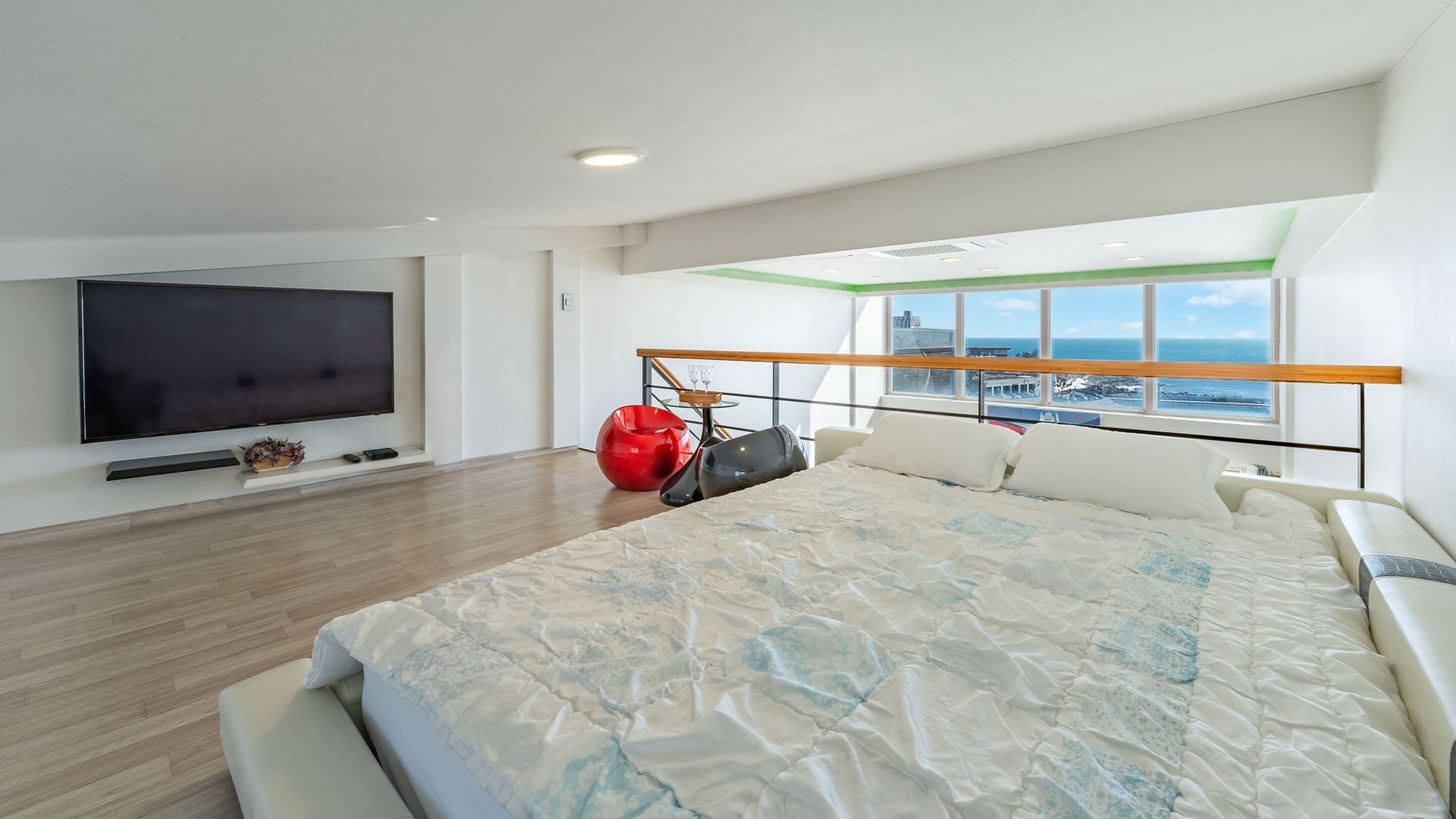 A modern hotel room with a large bed, a flat-screen TV, and a view of the sea through large windows.