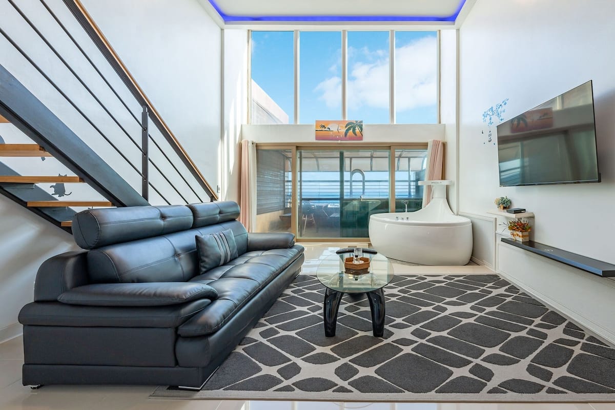 Ein modernes Wohnzimmer mit einer schwarzen Ledersofa, einem Glastisch und einem großen Fenster mit Blick auf das Meer.