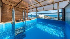 Una piscina interior con agua azul cristalina, paredes de madera y vistas al océano a través de amplios ventanales.