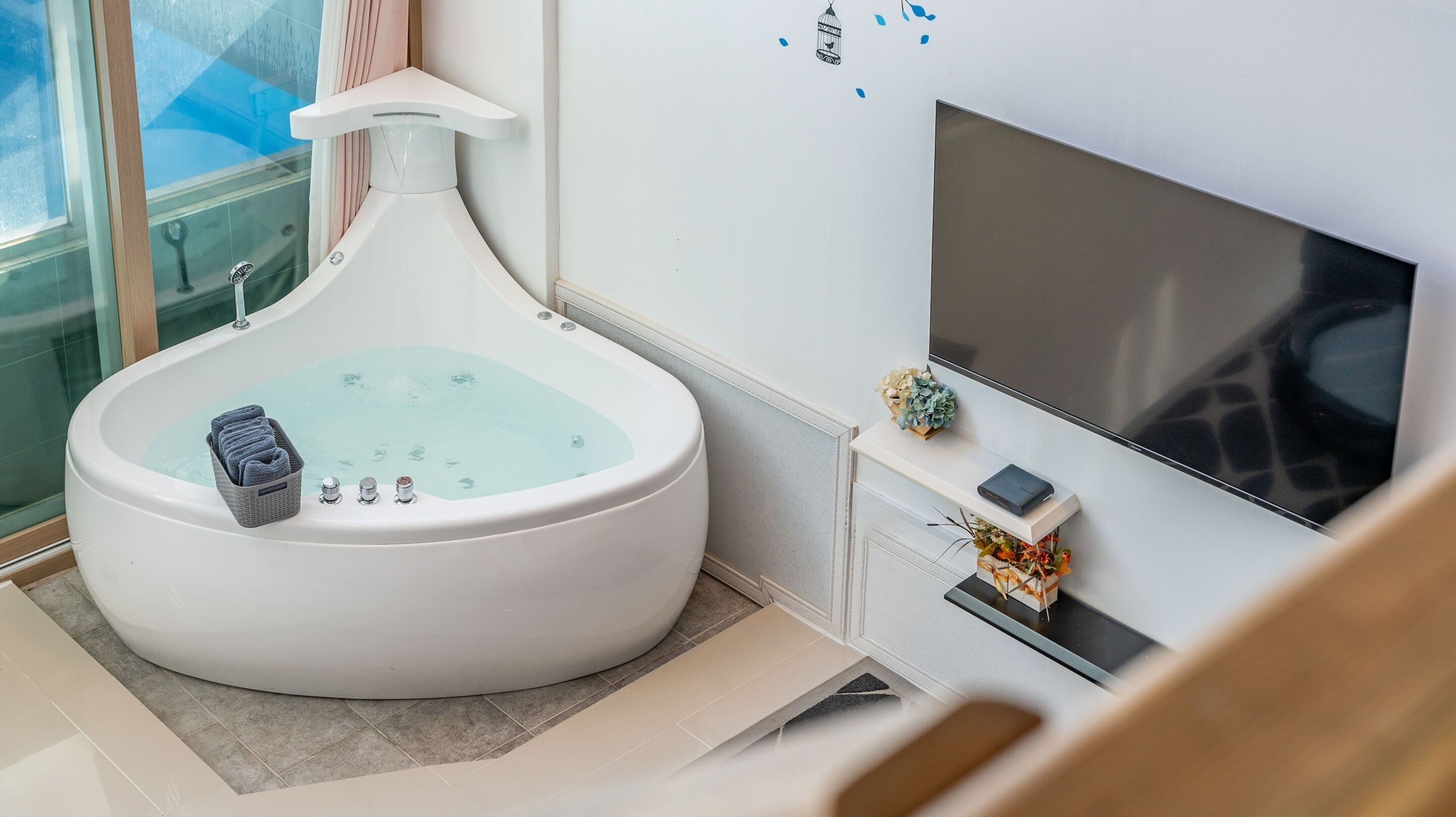 A modern bathroom with a large bathtub, a shower, and a flat-screen TV mounted on the wall.