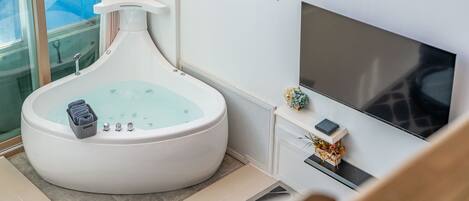 A modern bathroom with a large bathtub, a shower, and a flat-screen TV mounted on the wall.