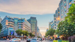 Uma rua urbana com edifícios de vários andares, alguns com placas de lojas.
