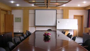 Uma sala de conferência com uma mesa comprida, cadeiras, uma tela de projetor e um quadro branco.