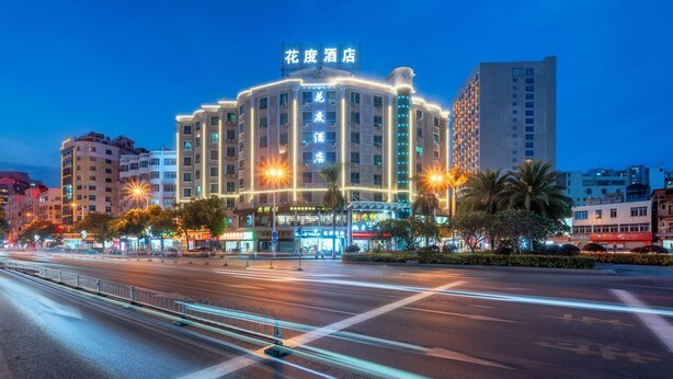 Um hotel de vários andares com sinalização iluminada, uma entrada bem iluminada e uma rua urbana ao redor.