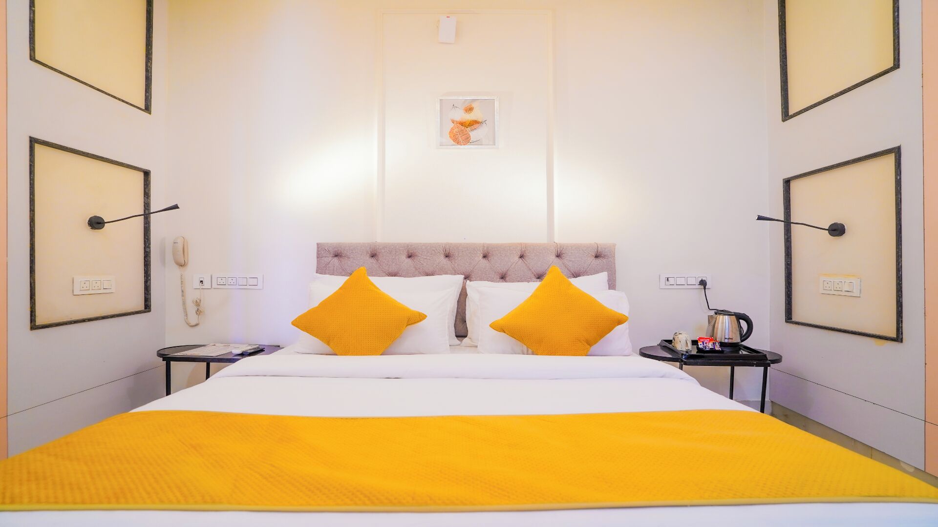 Habitación de hotel con cama, dos mesitas de noche, teléfono y un cuadro en la pared.