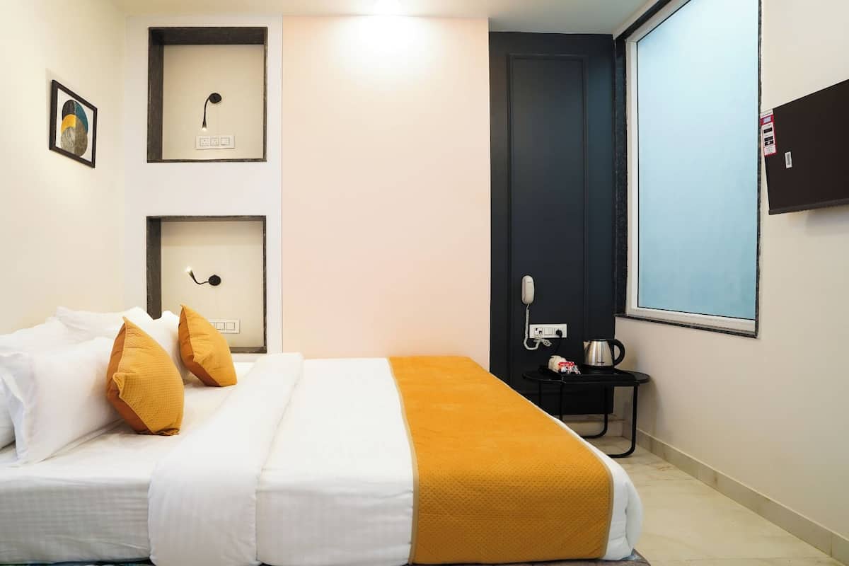 A hotel room with a bed, a bedside table with a kettle, a phone, and a window.