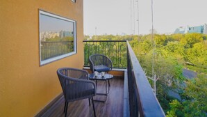 Een balkon met twee rieten stoelen en een kleine tafel, met uitzicht op een stadsgezicht en groen.