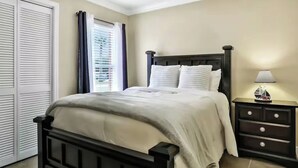 Un dormitorio con cama, mesita de noche y ventana con cortinas.