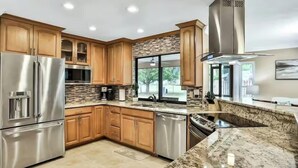 Una cocina moderna con armarios de madera, electrodomésticos de acero inoxidable, una encimera de granito y un ventanal amplio.