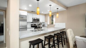 A modern kitchen with white cabinets, stainless steel appliances, and a bar area with stools.
