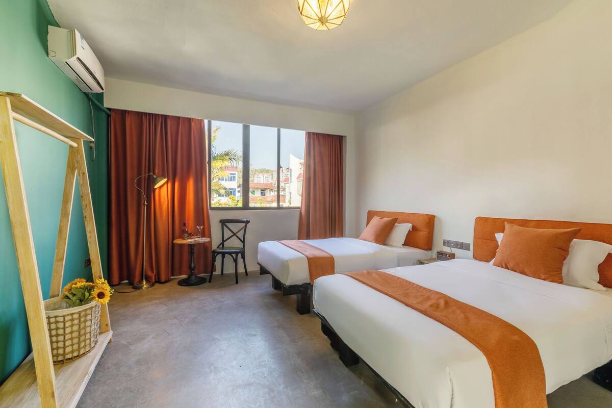 Een hotelkamer met twee bedden, een bureau, een stoel en een raam met gordijnen.