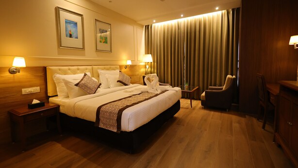 A hotel room with a large bed, two bedside tables with lamps, a chair, a desk, and a ceiling fan. - Hotel Aashray Inn  (Hubli)