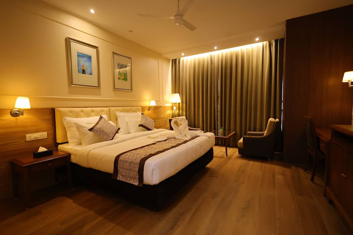 A hotel room with a large bed, two bedside tables with lamps, a chair, a desk, and a ceiling fan.