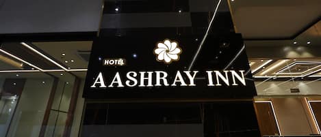 A hotel sign with the name "AASHRAY INN" and a logo.