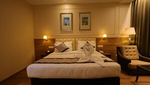 A hotel room with a large bed, two wall-mounted lamps, a chair, and two framed artworks on the wall.