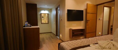 A hotel room with a bed, a television, a desk with a chair, and a mirror.