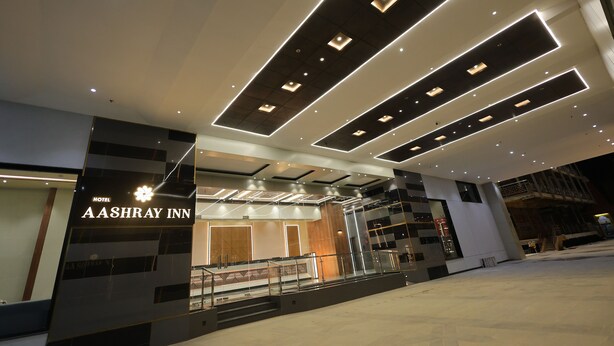 A modern hotel entrance with a prominent sign for Aashray Inn, featuring a geometric ceiling design and a glass facade.