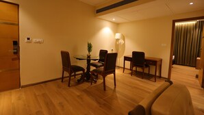 A hotel room with a wooden floor, a dining table with chairs, a lamp, and a desk with a chair. - Hotel Aashray Inn  (Hubli)