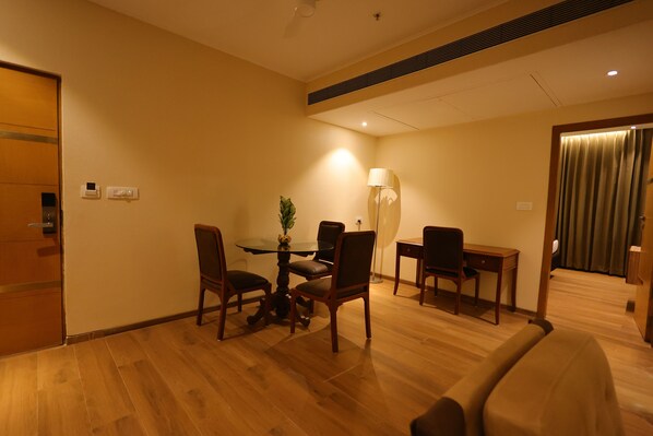 Une chambre d’hôtel avec un plancher en bois, une table à manger avec des chaises, une lampe et un bureau avec une chaise.
