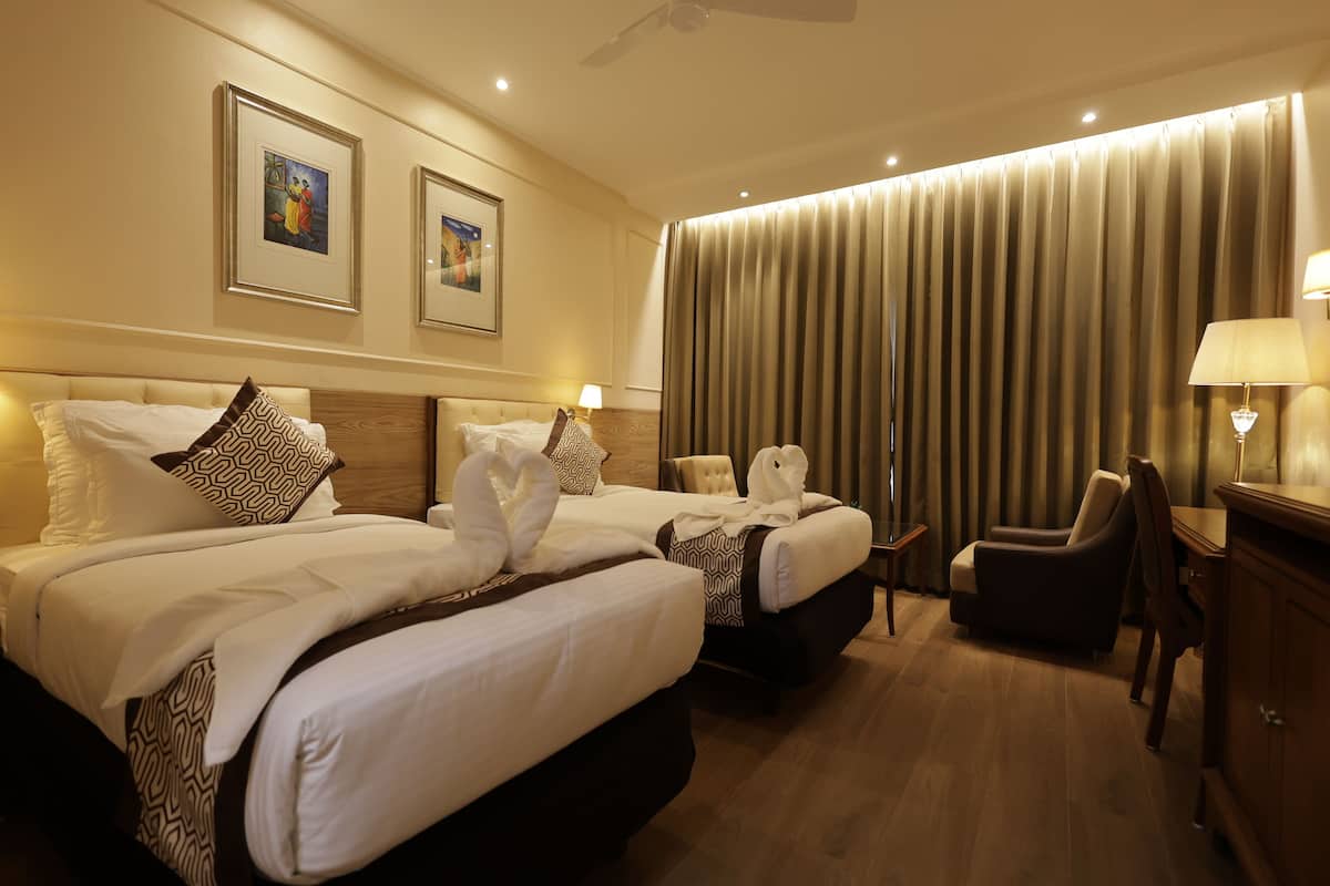 A hotel room with two beds, a desk, a chair, a lamp, and a large window with curtains.