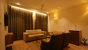 A living room with a sofa, armchair, and coffee table. There is a ceiling fan, a television mounted on the wall, and a cabinet. - Hotel Aashray Inn  (Hubli)
