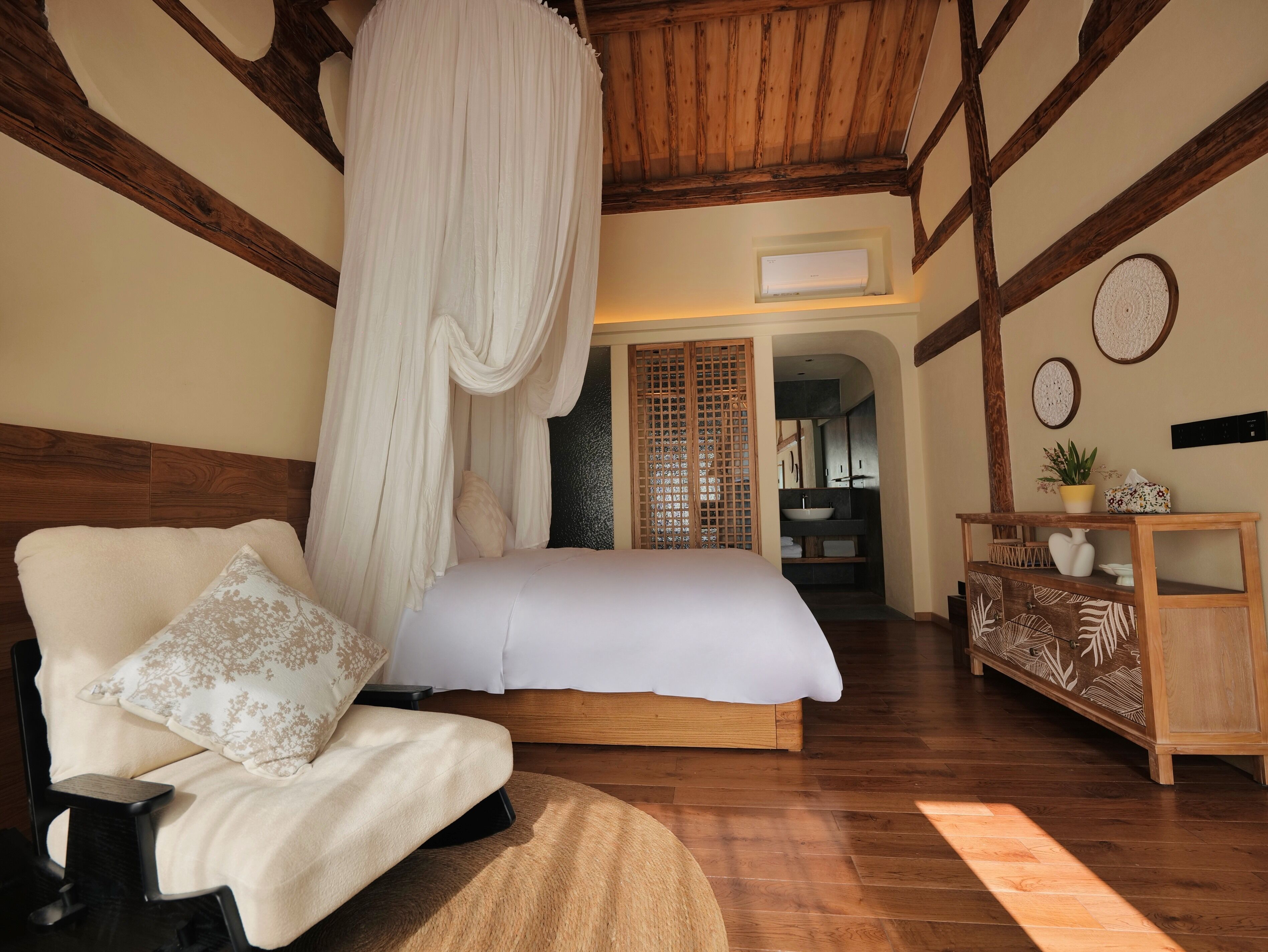 A bedroom with a large bed, a wooden headboard, a bedside table, a chair, a canopy, and a wooden cabinet.