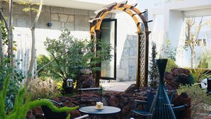 Un patio con muro de piedra, un arco de madera y mobiliario para exteriores.
