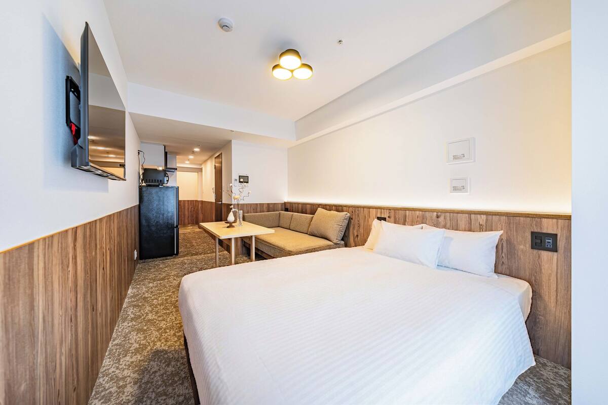 Une chambre d’hôtel avec un grand lit, un coin salon, une petite table, un téléviseur fixé au mur et un luminaire au plafond.