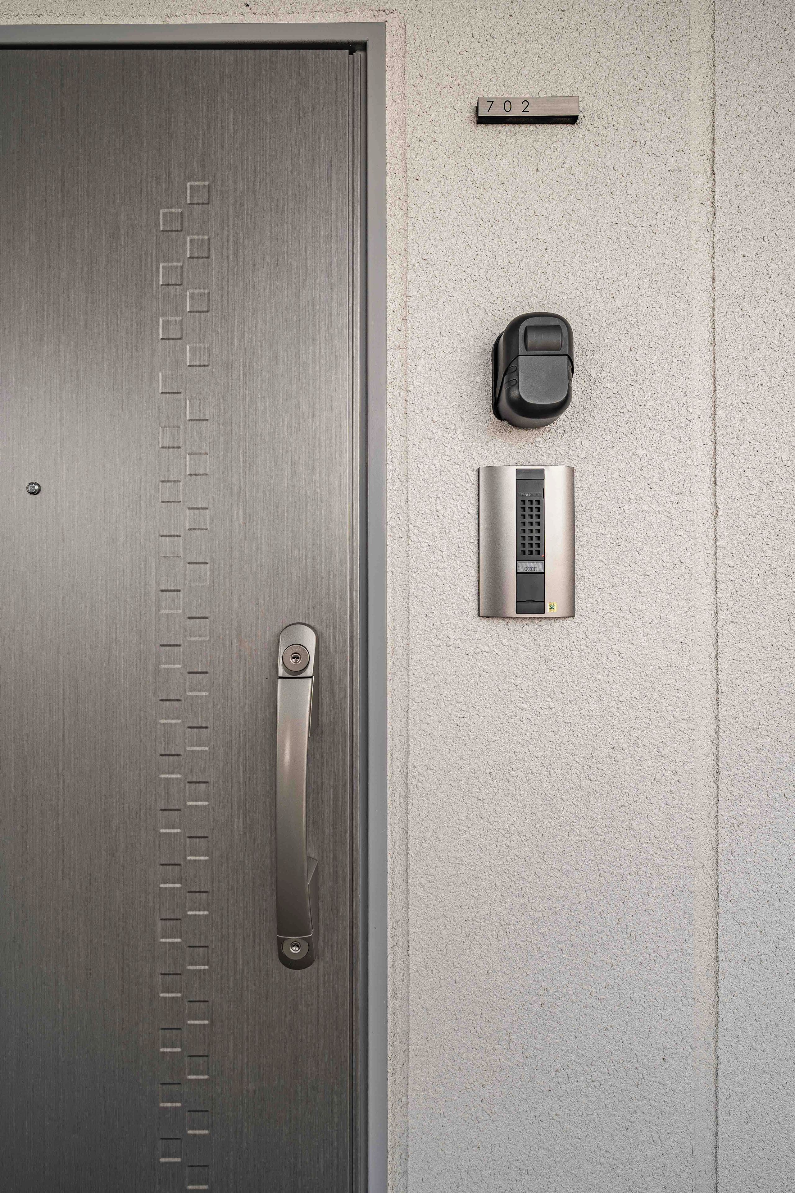 A modern door with a keypad lock, a small mailbox, and a number plate above it.