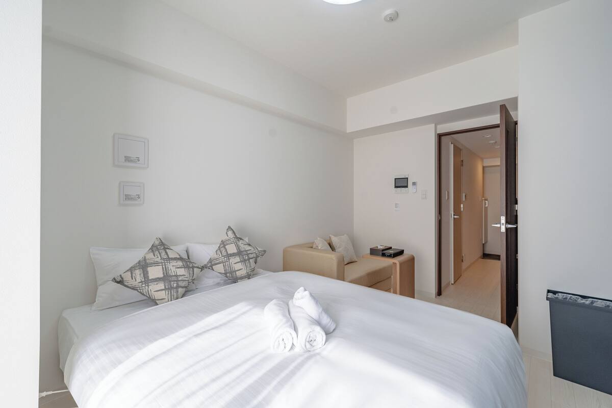 Une chambre d’hôtel avec un lit bien fait, une petite table de chevet et une porte donnant sur une autre pièce.