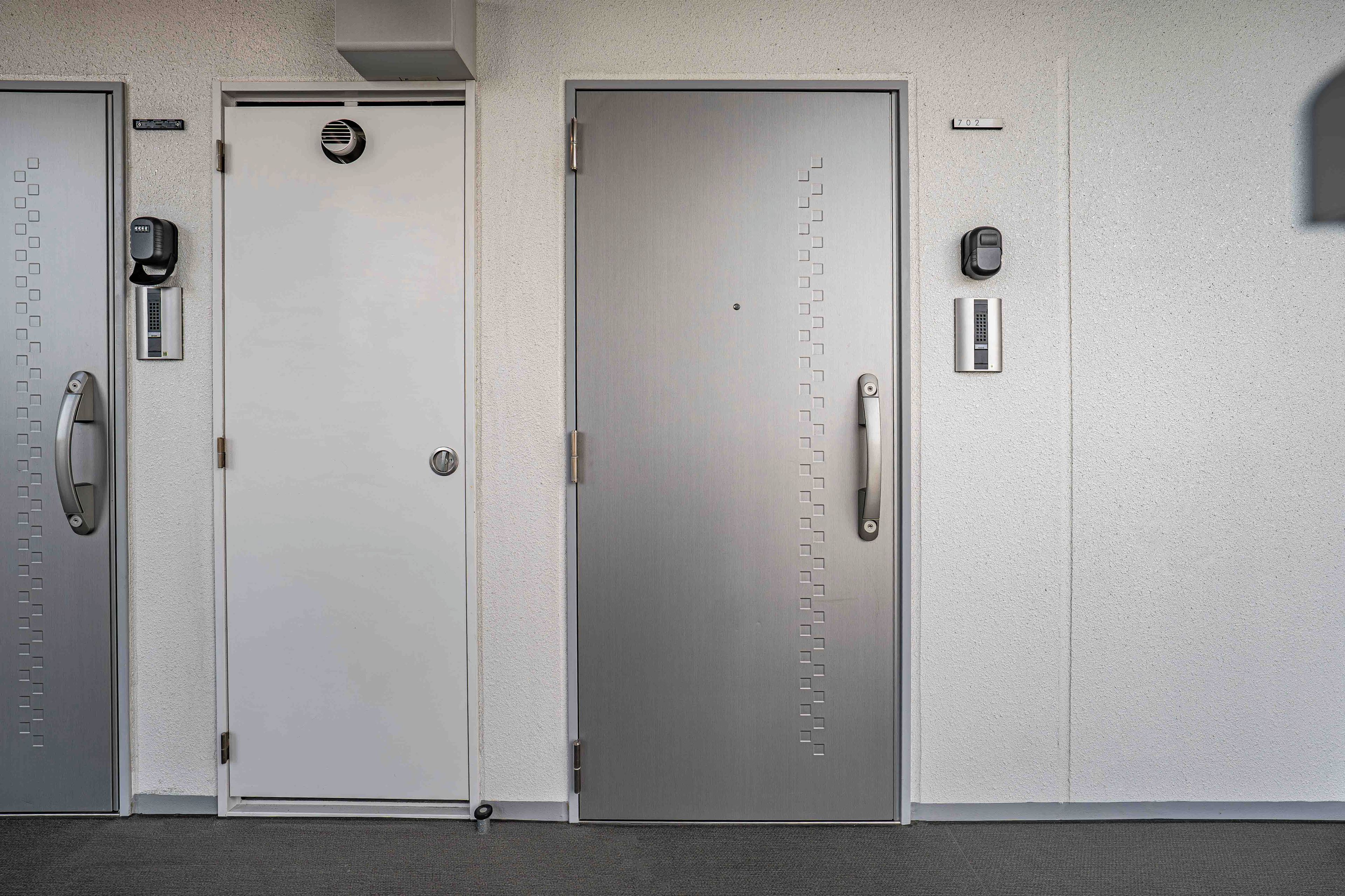 Three doors with intercoms and a number plate.