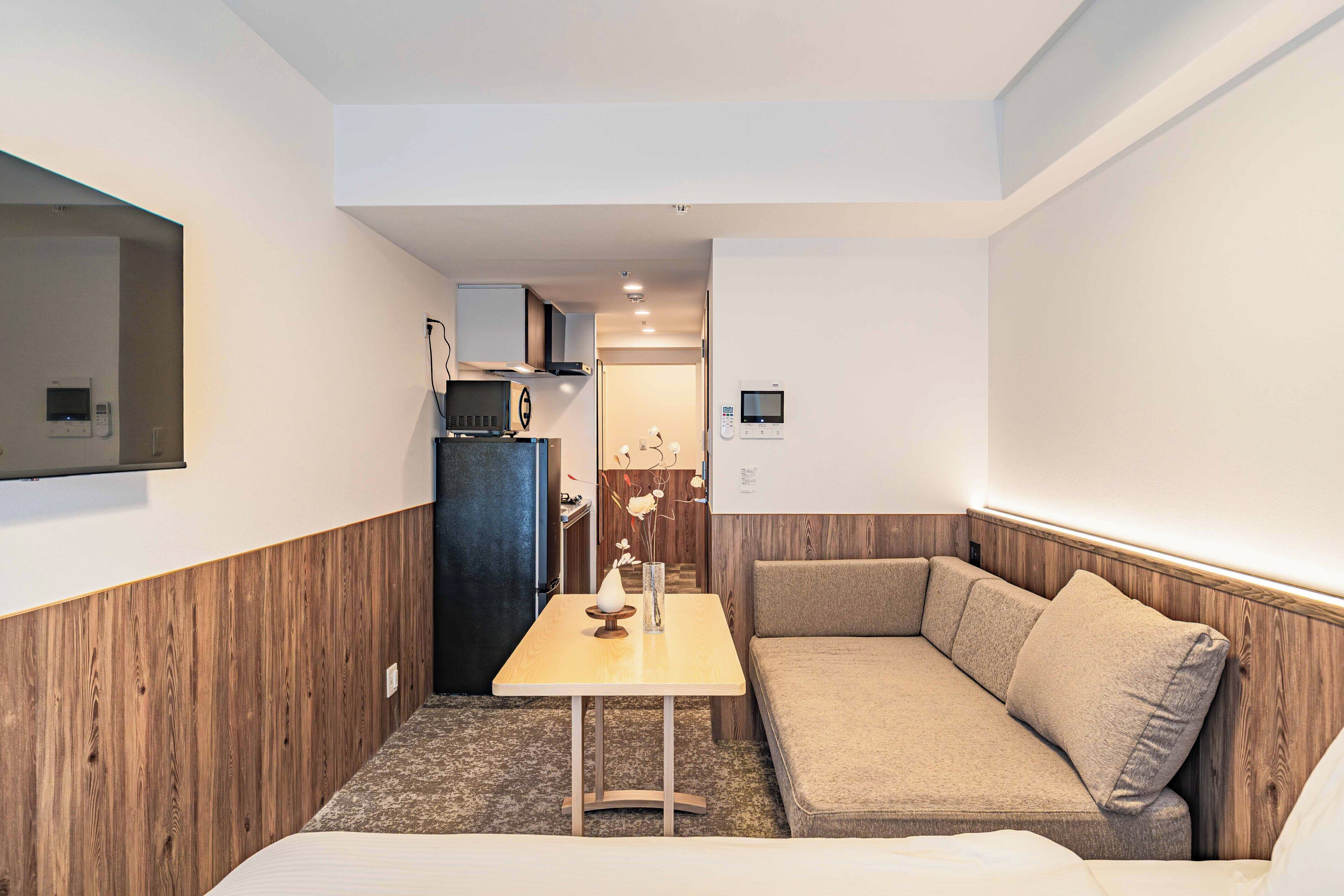 A compact hotel room with a kitchenette, a sofa, a small table, and a bed.