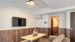 Camera d'hotel moderna con parete decorata in legno, televisore a schermo piatto montato a parete, un tavolino con un vaso e oggetti decorativi, e un divano.