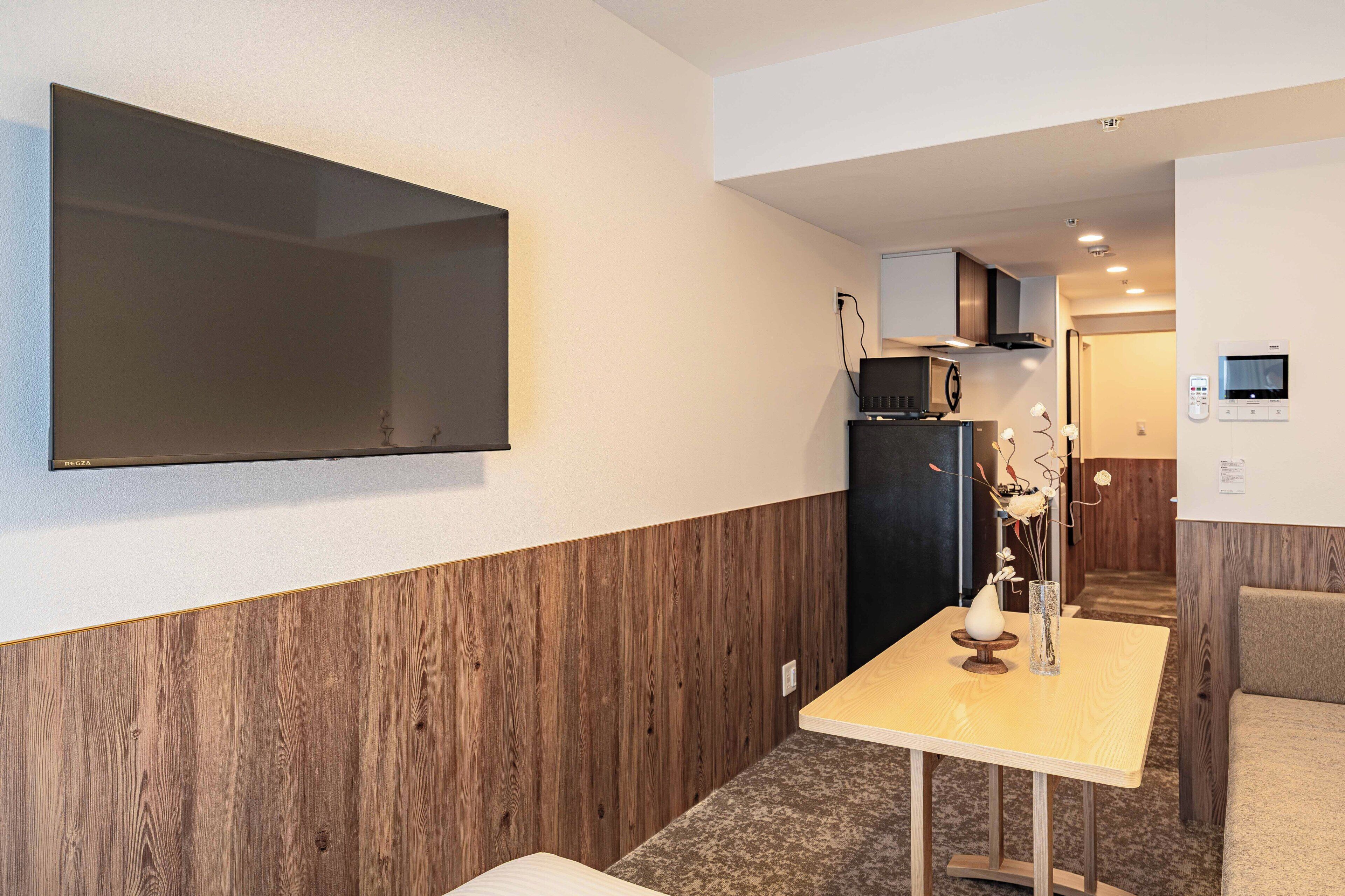 A modern kitchen with a flat-screen TV, a microwave, and a dining area with a table and chairs.