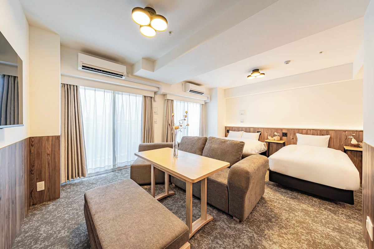 Une chambre d’hôtel avec un lit, un canapé, une petite table et une fenêtre avec des rideaux.
