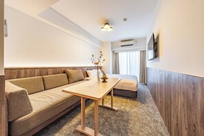 Habitación de hotel con sofá, una mesa de madera, un jarrón decorativo, un equipo de aire acondicionado y un televisor fijado a la pared.
