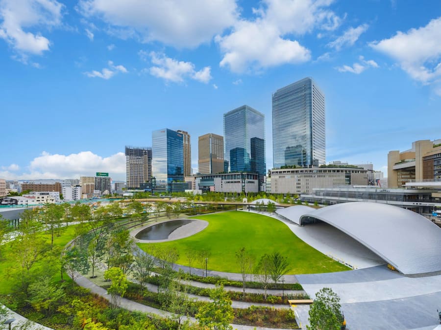 Un paisaje urbano moderno con edificios altos, un parque verde central y un distintivo elemento arquitectónico curvo.